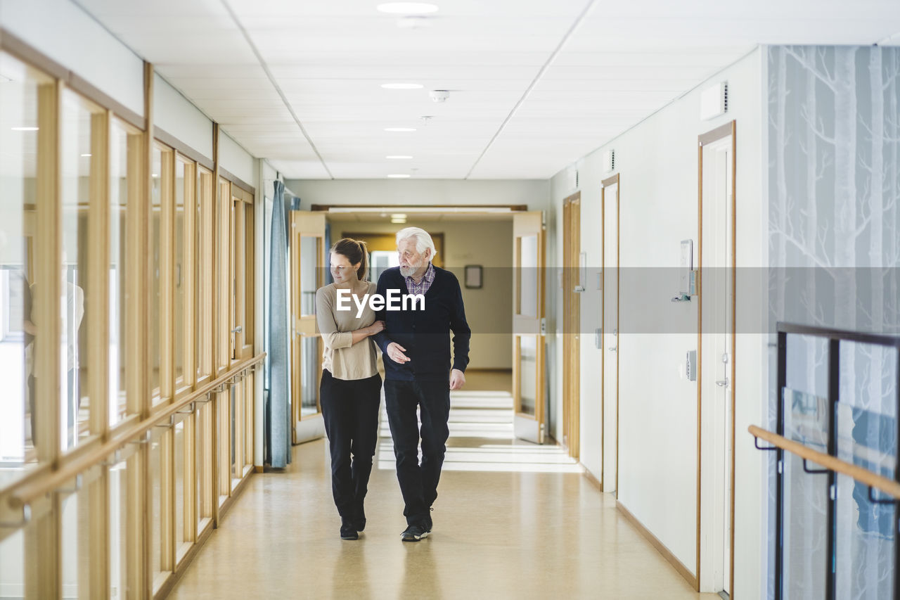 Young woman looking away while walking with grandfather in corridor at nursing home