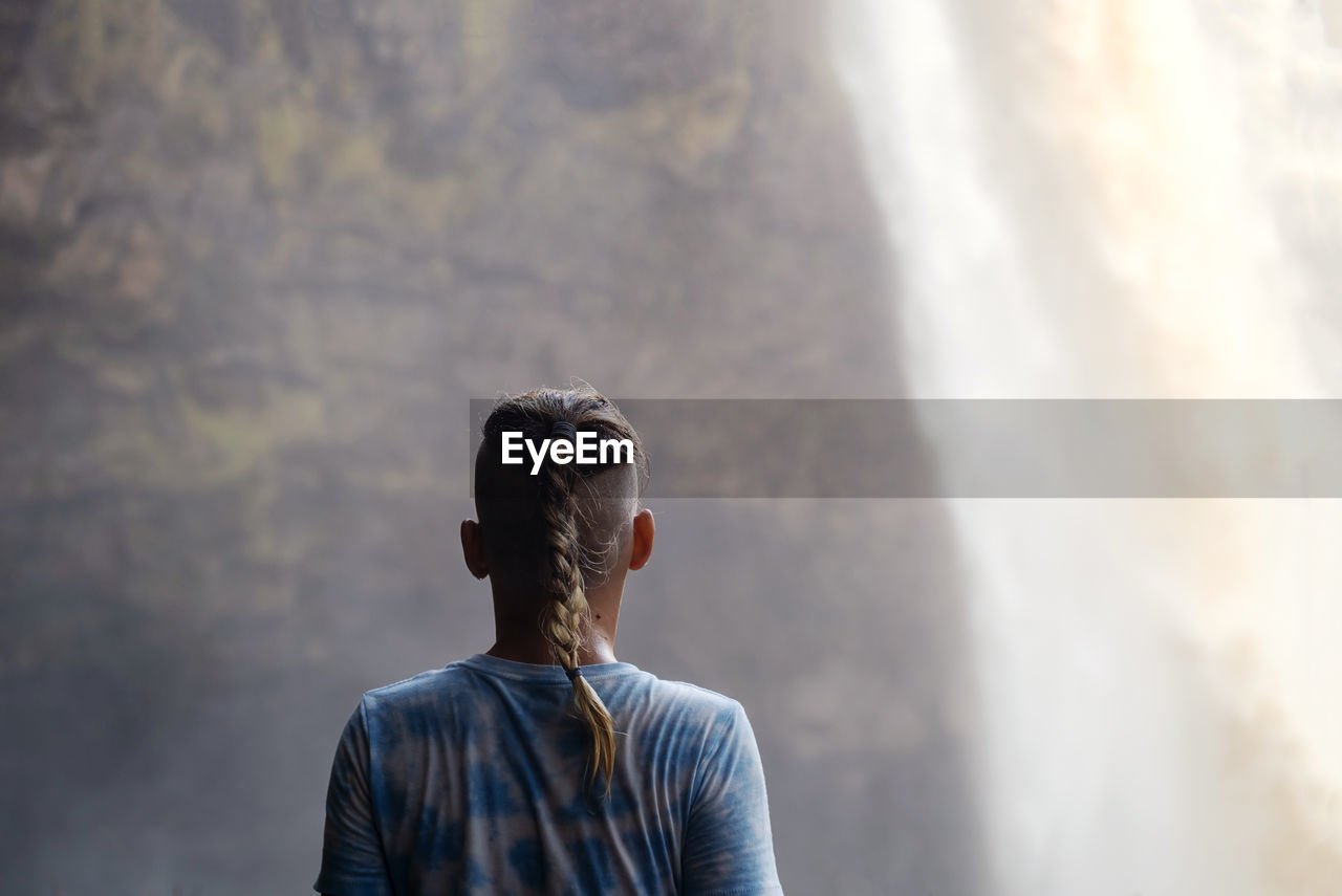 Teenager looking as waterfall cascades in front of him.