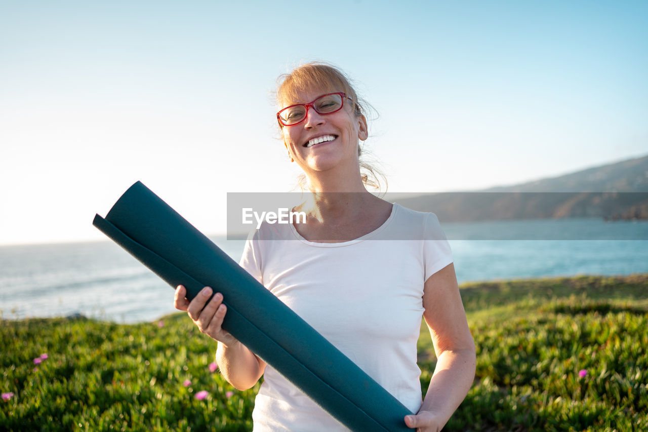 portrait of young woman using mobile phone while standing against sky