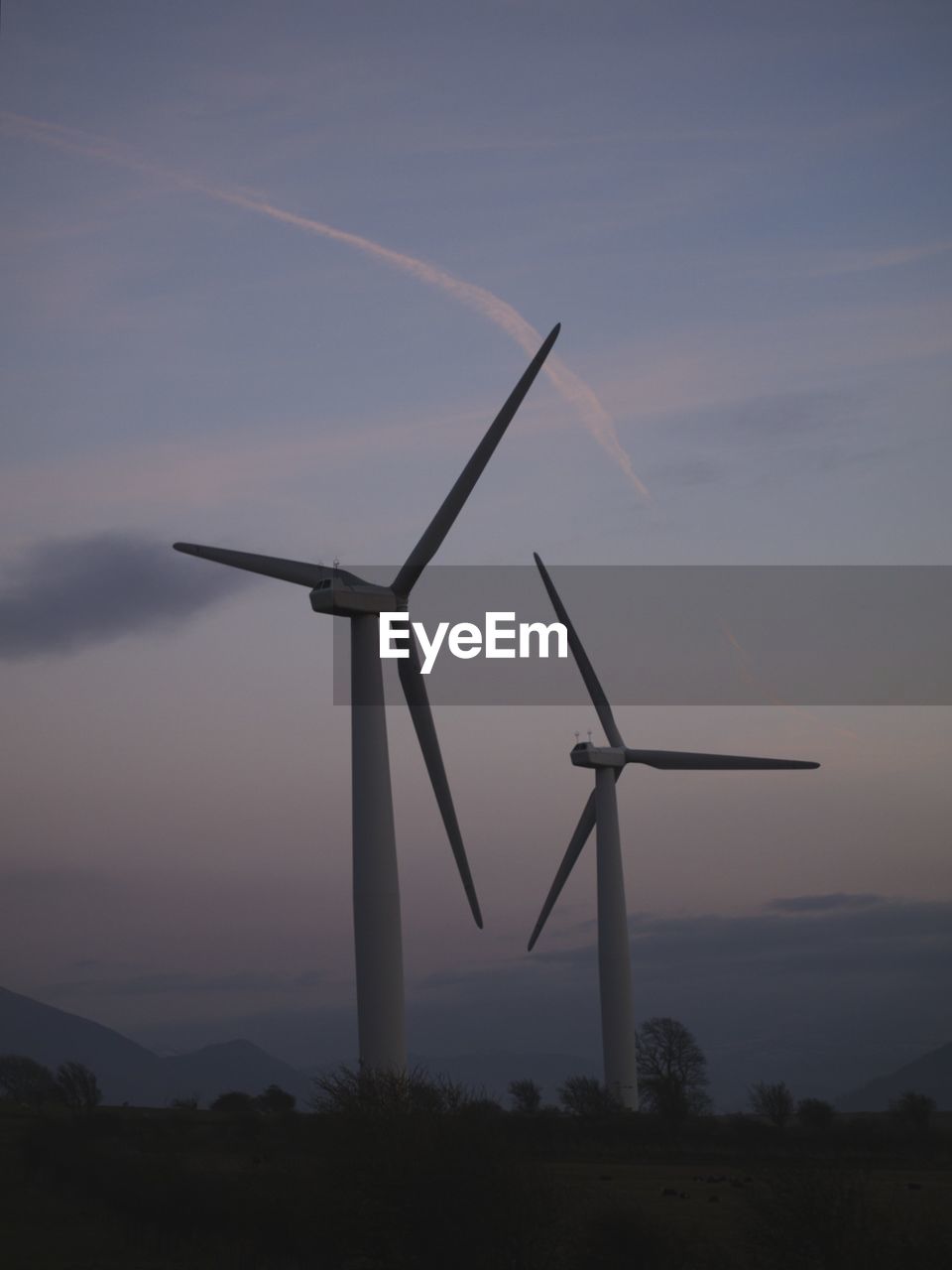 Windmills on landscape against sky during sunset