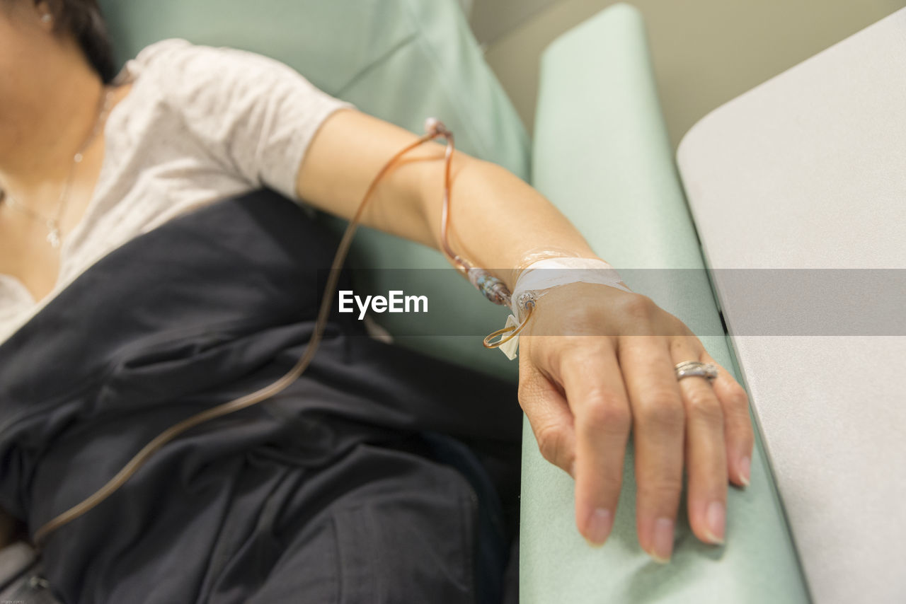 Cropped hand of woman with iv drip on bed in hospital