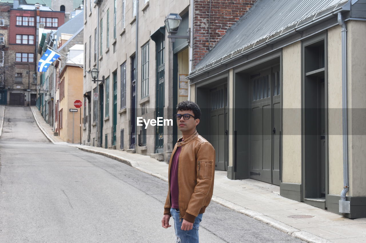 Portrait of young man standing on street against buildings