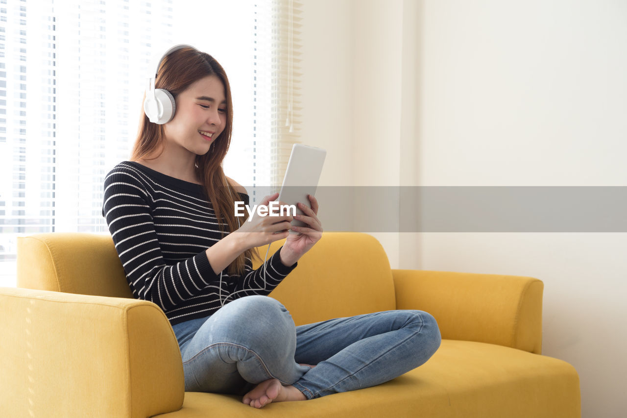 Young woman using digital tablet while sitting on sofa