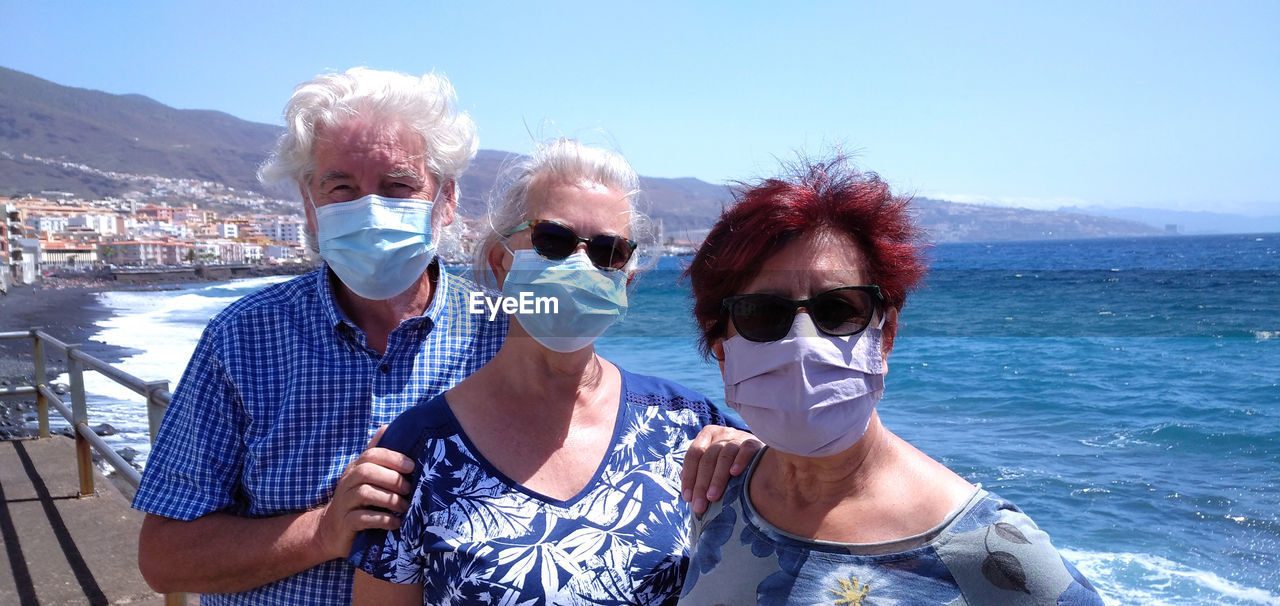 Portrait of friends wearing mask at beach against sky