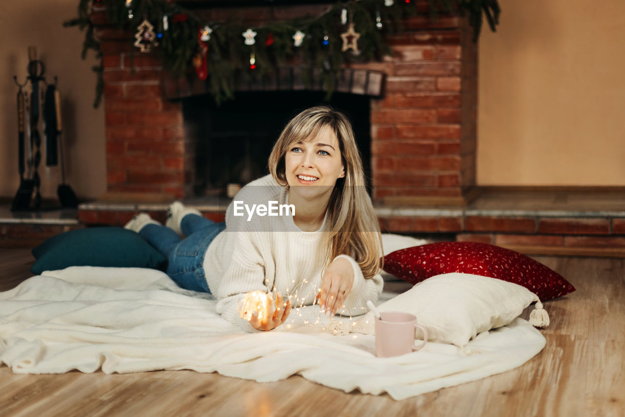 A charming young woman lies on a rug by the fireplace on christmas eve