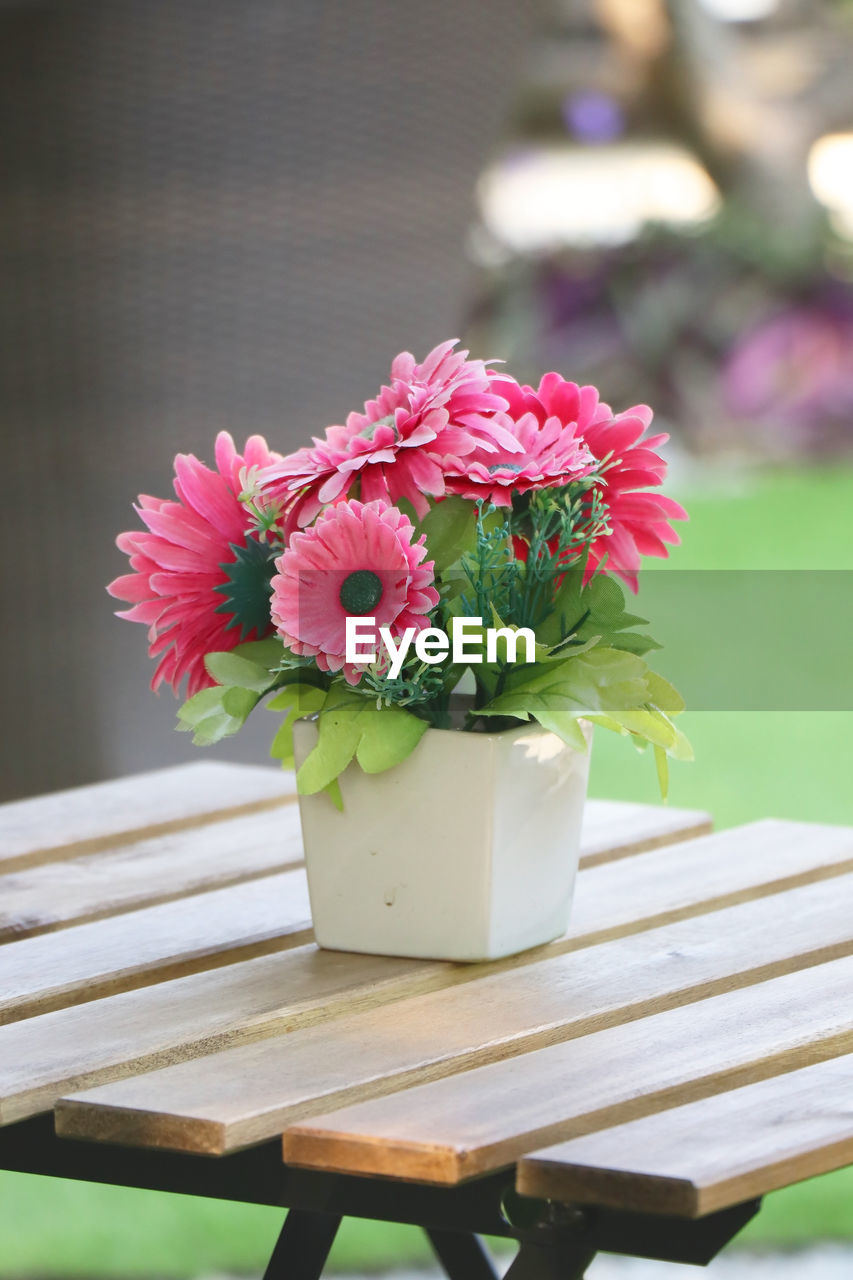 Pink artificial flower in white pot on wooden dining table