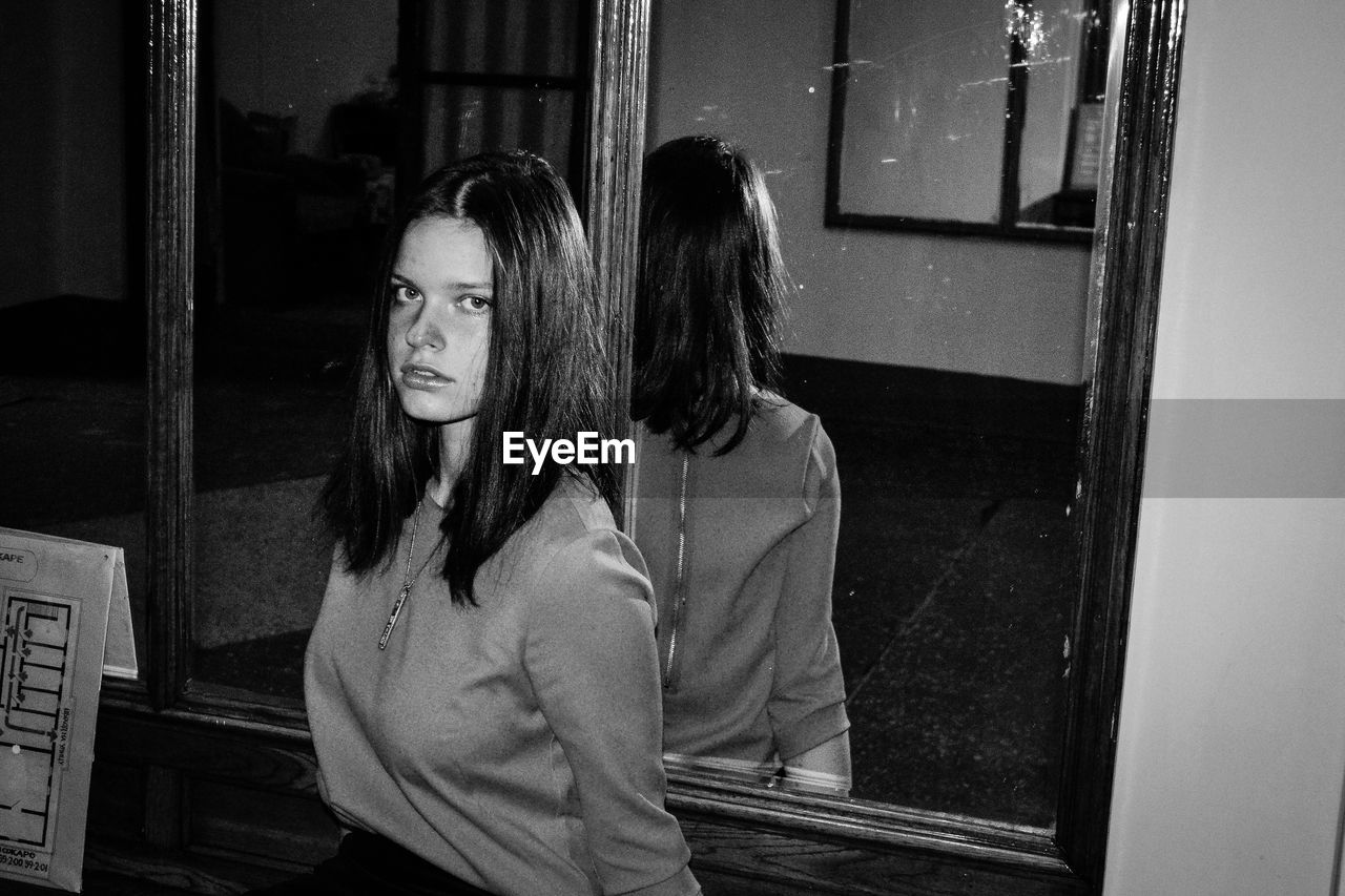 Portrait of young woman standing against mirror at home