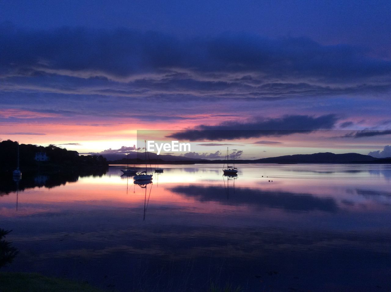 Scenic view of loch  against dramatic sky during sunset