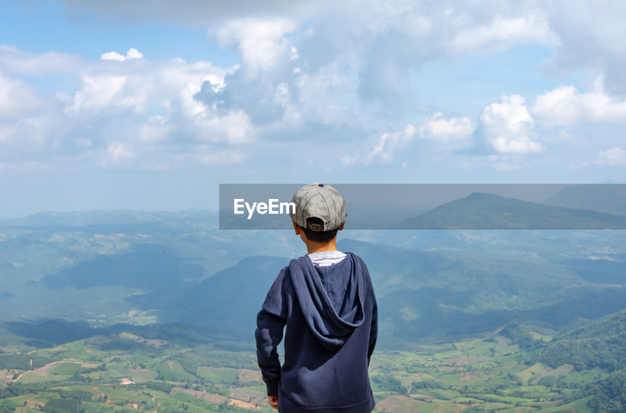 Rear view of boy standing against mountains and sky