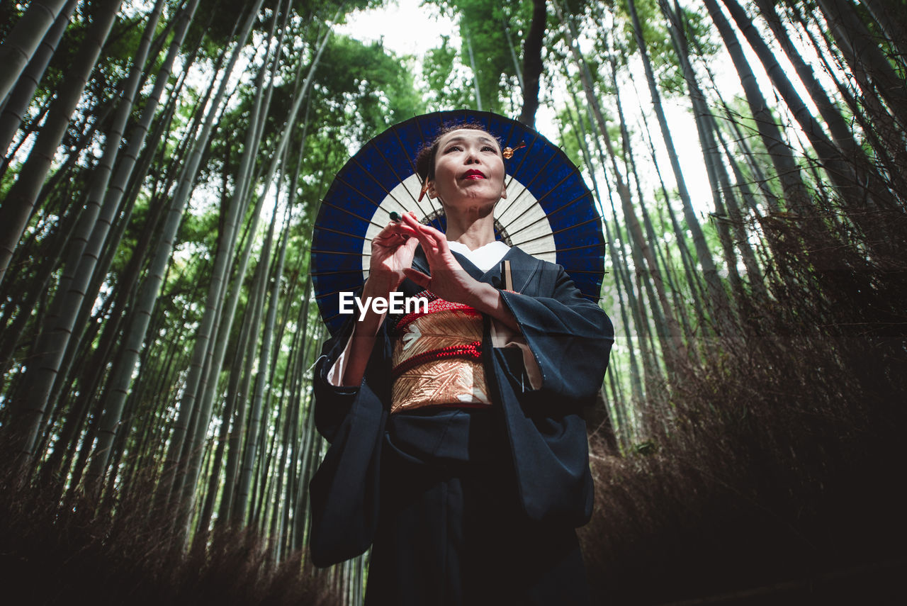 Mature woman with umbrella standing amidst trees