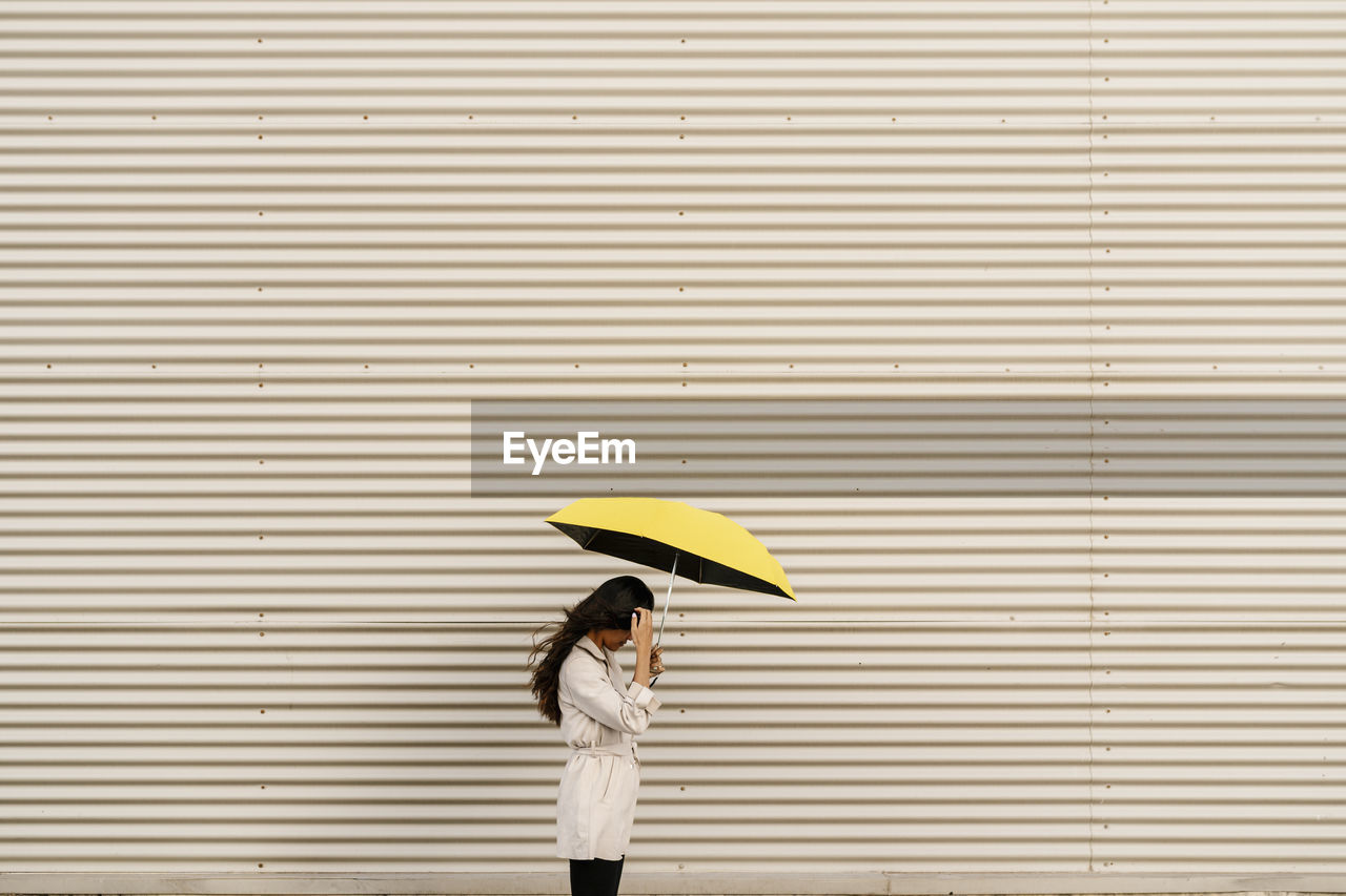 Woman holding umbrella by white corrugated wall