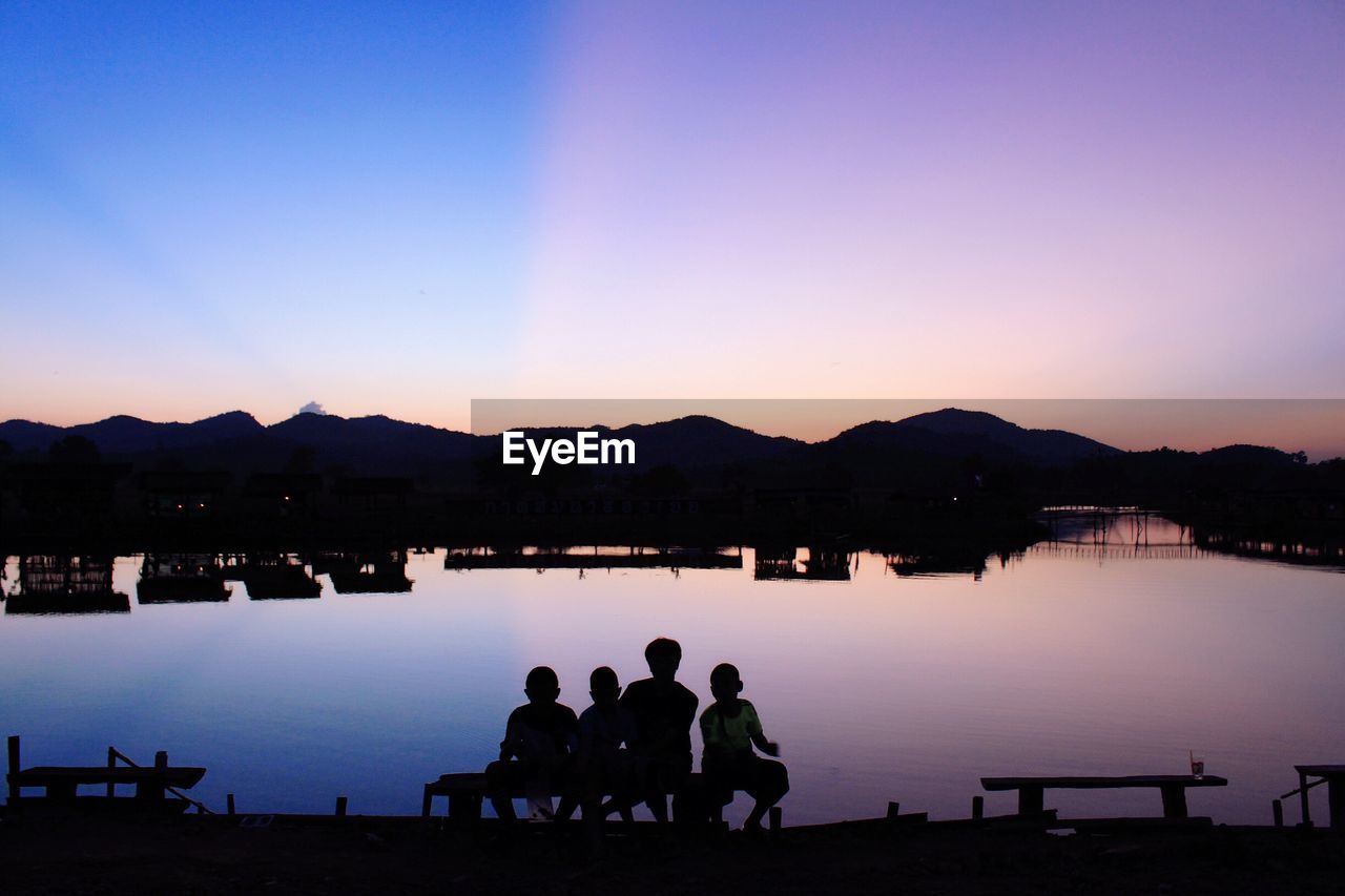 SILHOUETTE PEOPLE SITTING ON LAKE AGAINST CLEAR SKY