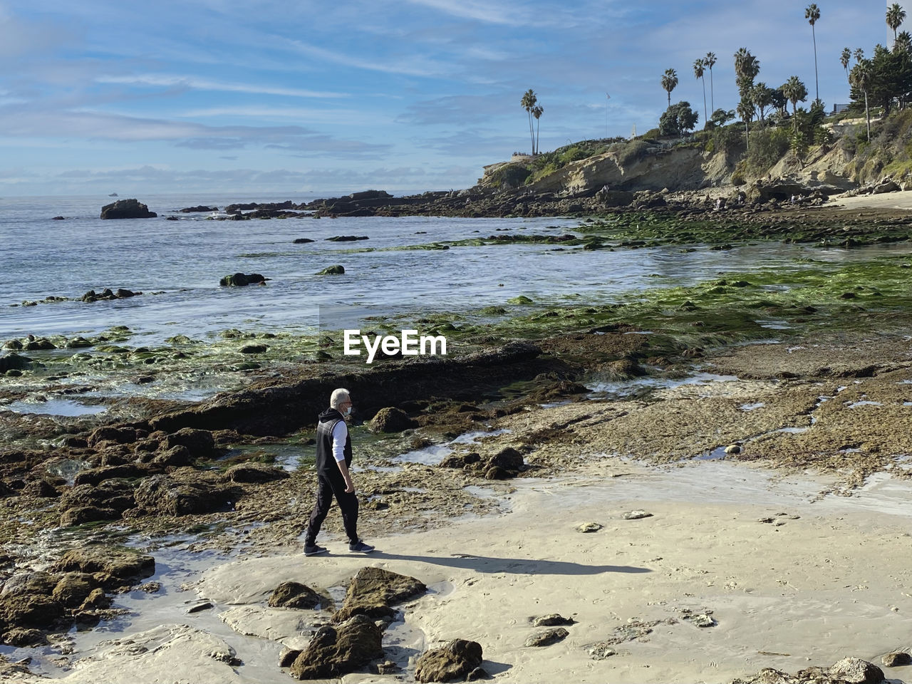 Man walking on rocky beach against sky