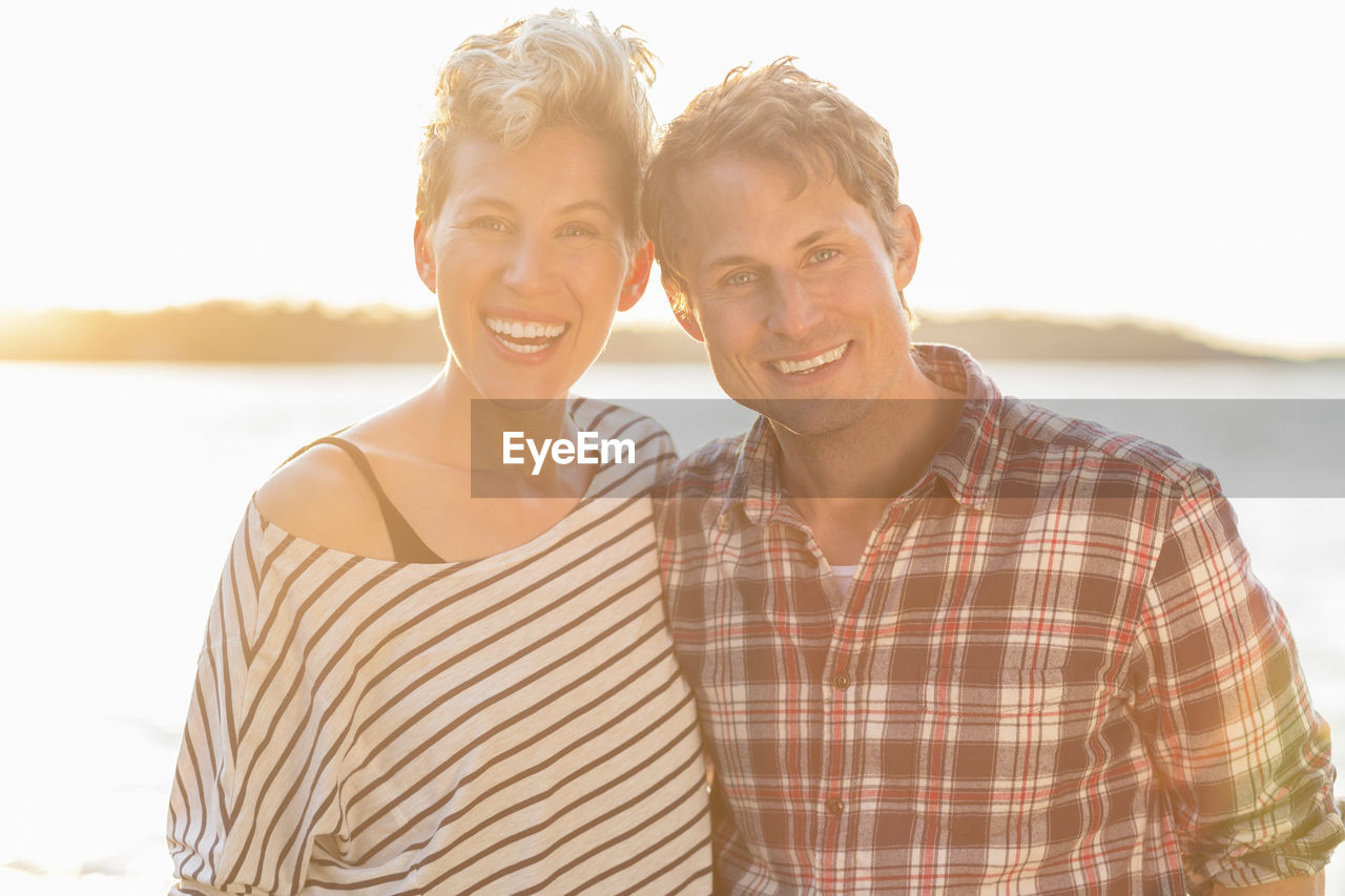 Portrait of happy couple standing on beach during sunset