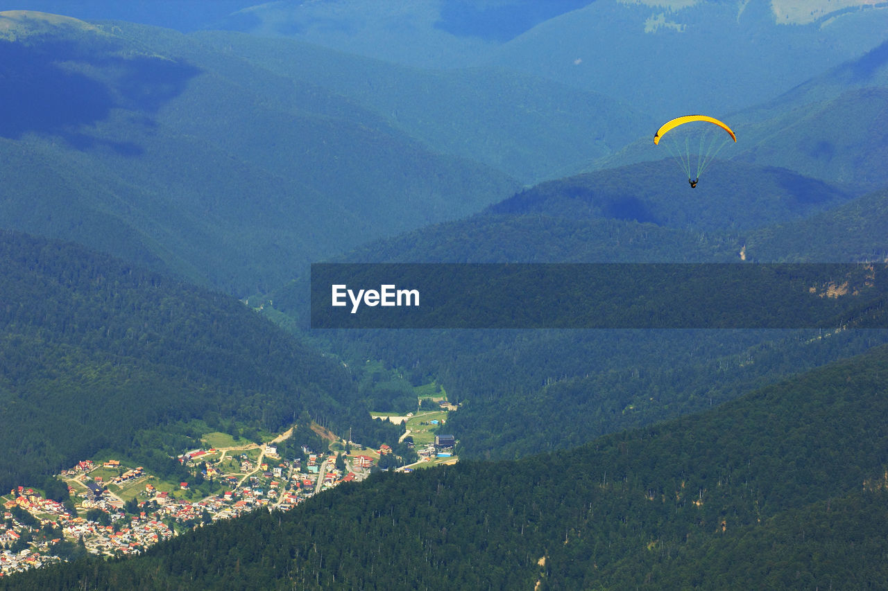 High angle view of person paragliding above green mountains