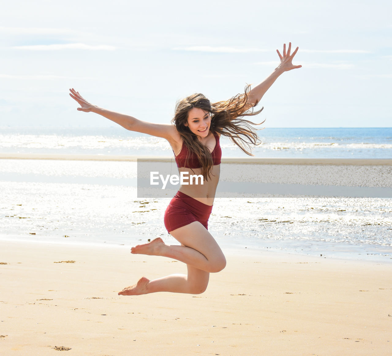 YOUNG WOMAN WITH ARMS RAISED ON BEACH