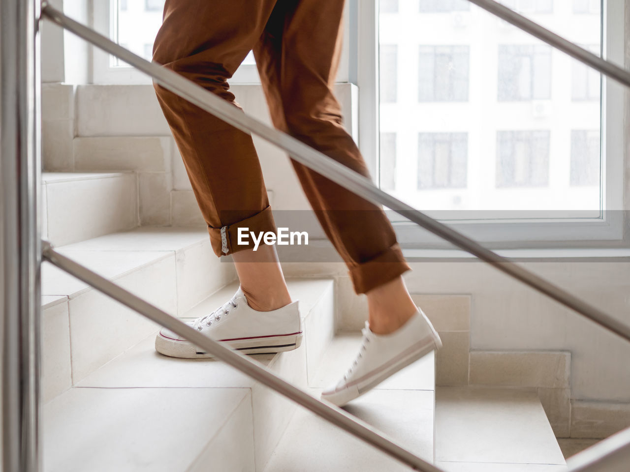 Woman in white sneakers and khaki trousers goes upstairs to her apartment.  staircase in building. 