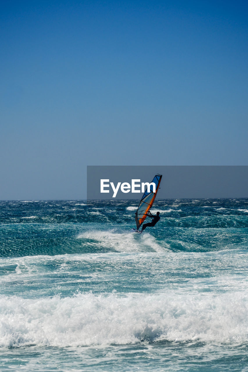 Silhouette man surfing in sea against clear blue sky