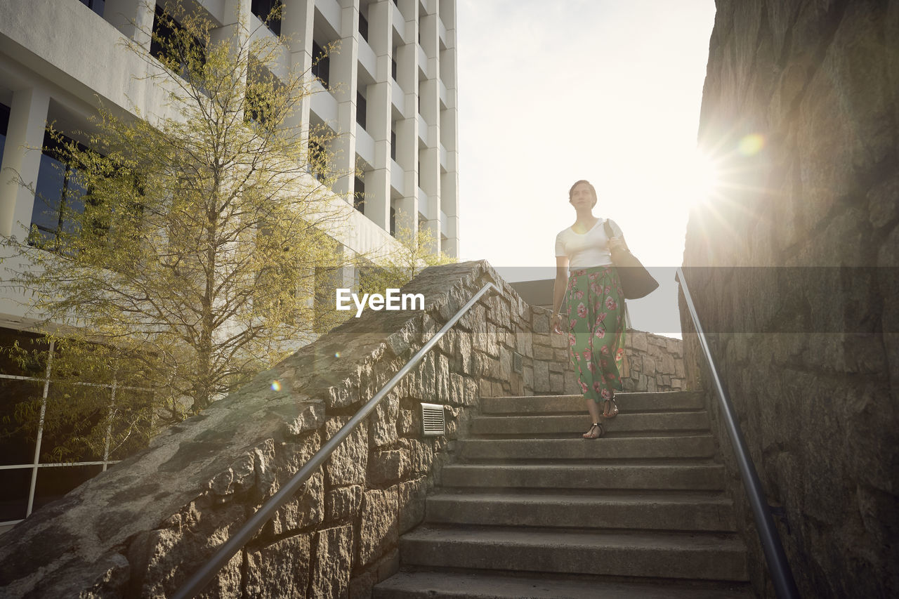 Low angle view of woman moving down on steps against sky during sunny day