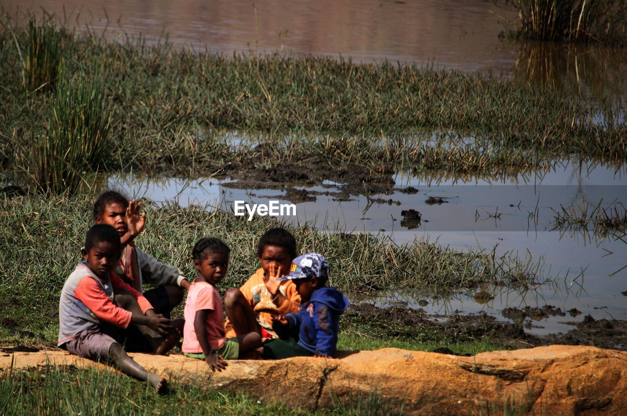 REAR VIEW OF PEOPLE SITTING ON SHORE