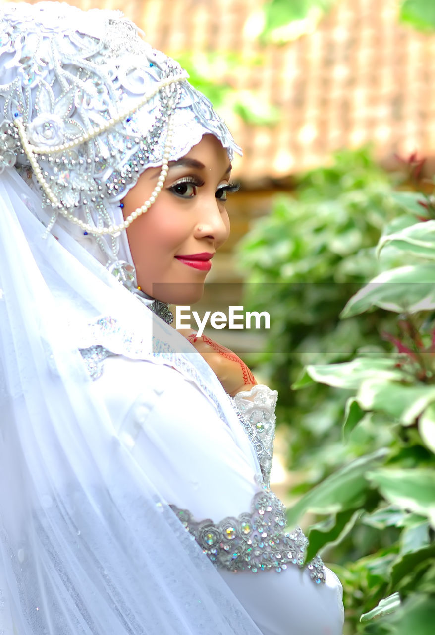 Smiling young woman standing by plants