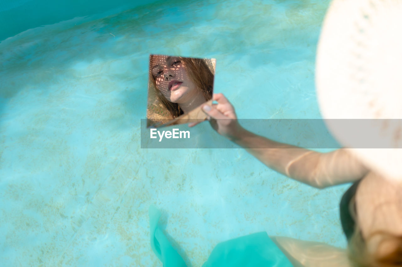 Reflection of woman in mirror while sitting in swimming pool