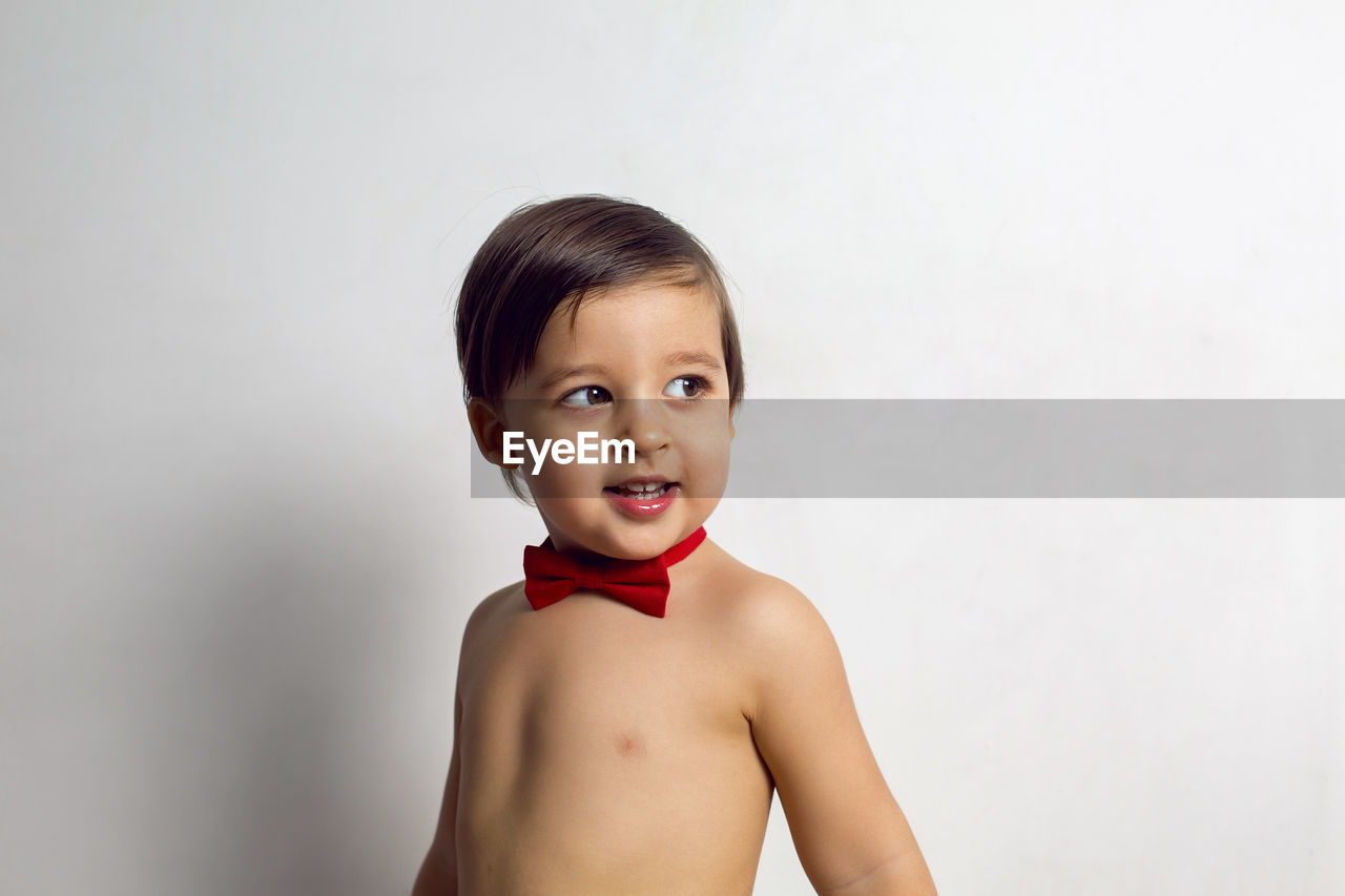 Child without a t-shirt sitting on a white background with a red bow tie