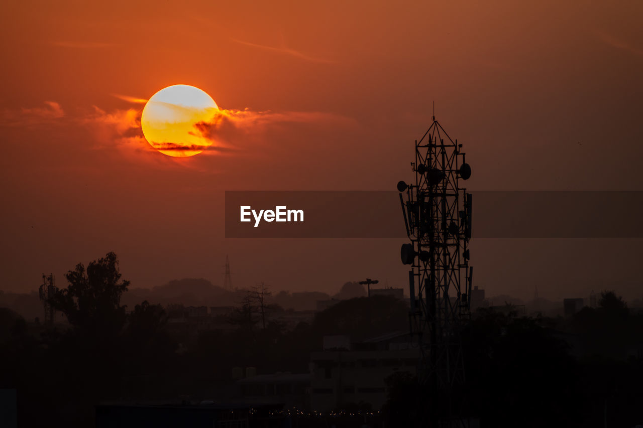 Communication tower silhouetted against orange sky at sunset in chittaurgarh, india