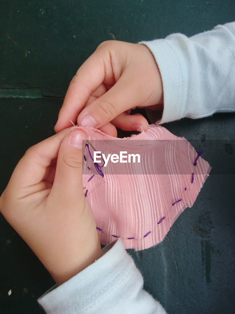 Cropped hands of child stitching fabric on table