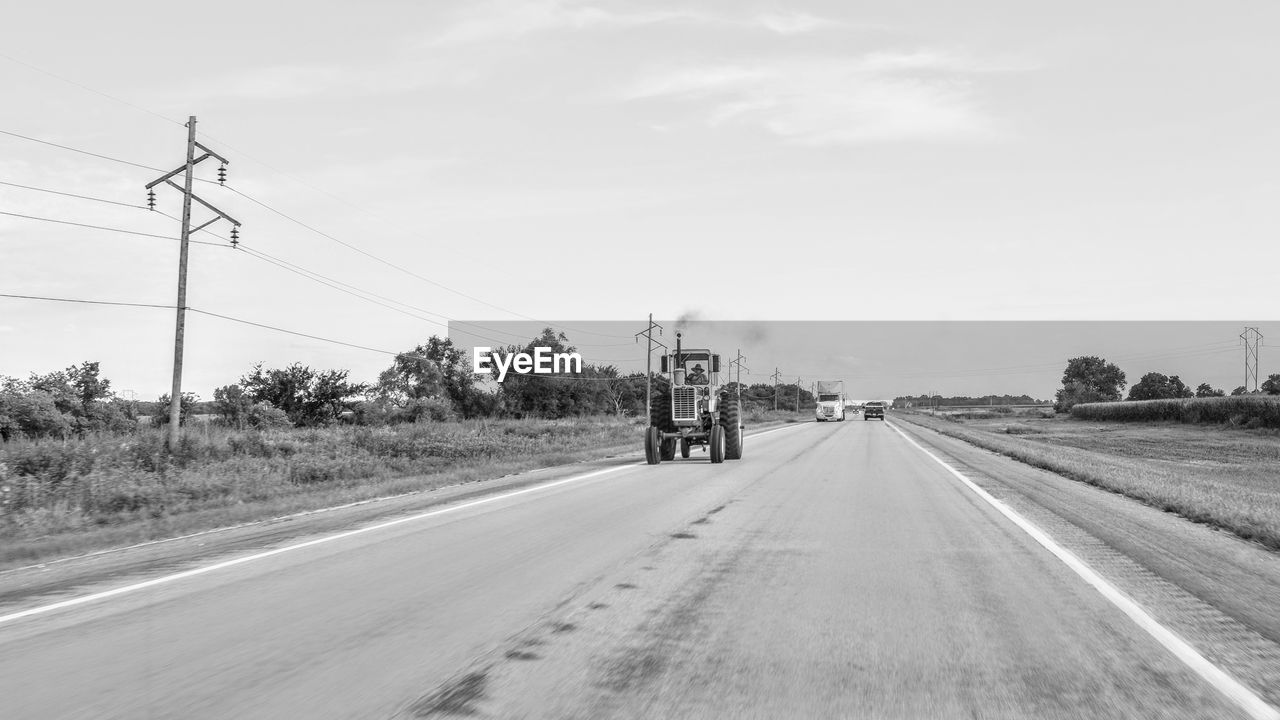 Person driving tractor on road against sky