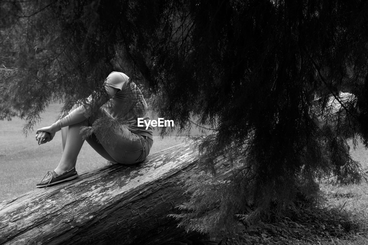 Side view of woman sitting on fallen tree