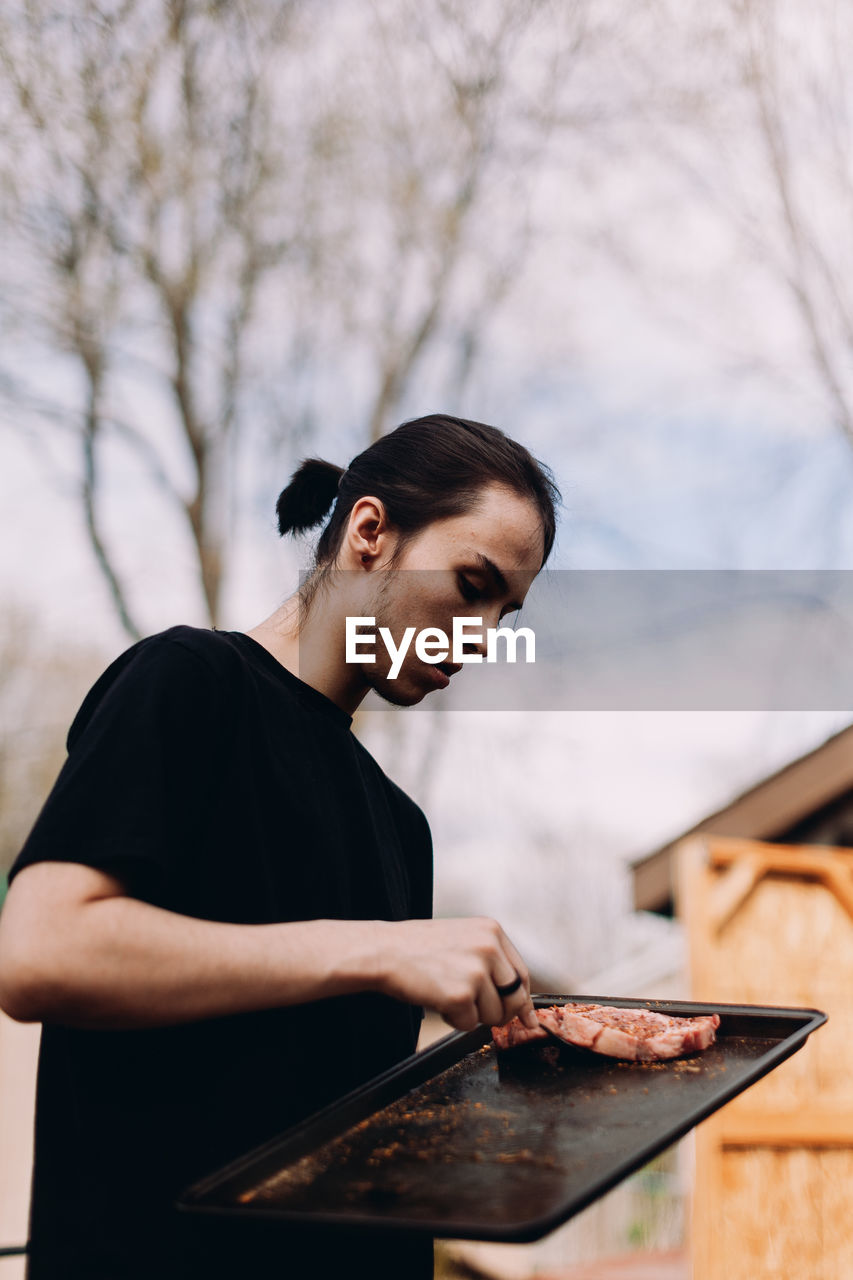 Young male adult placing steaks on barbecue.