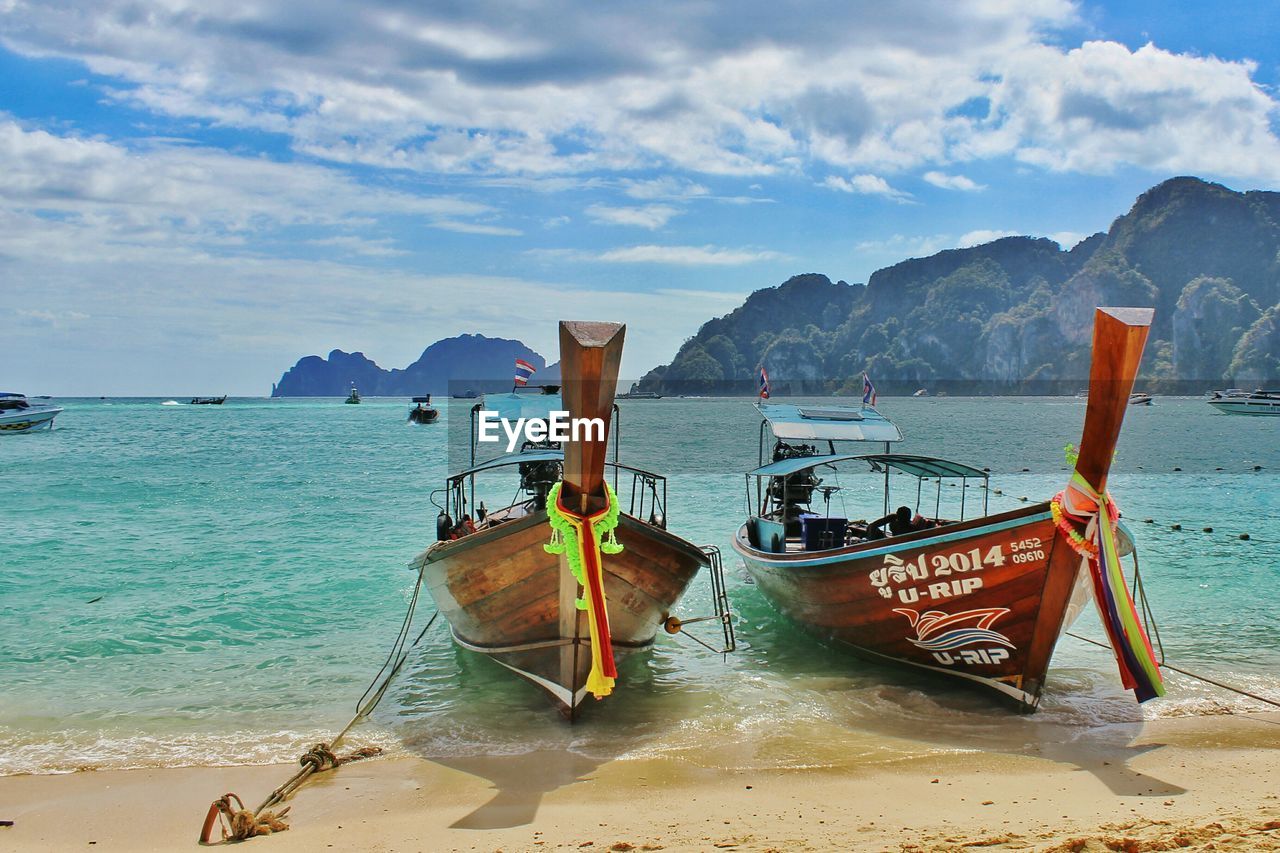 Longtail boats moored on shore against sky