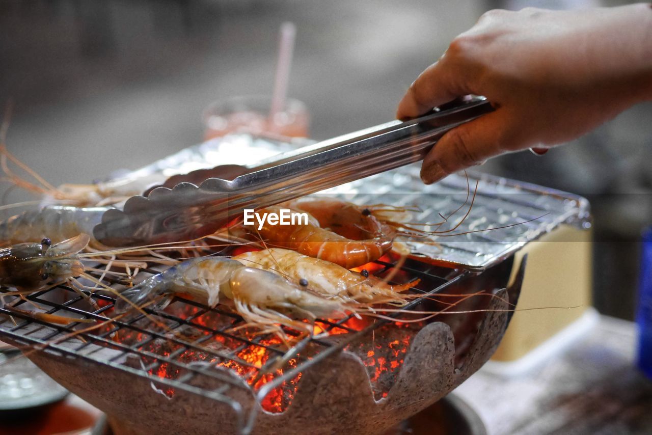 cropped hand of man preparing food on barbecue grill