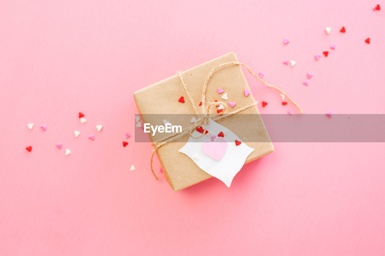 High angle view of brown paper gift white white note and hearts on pink background