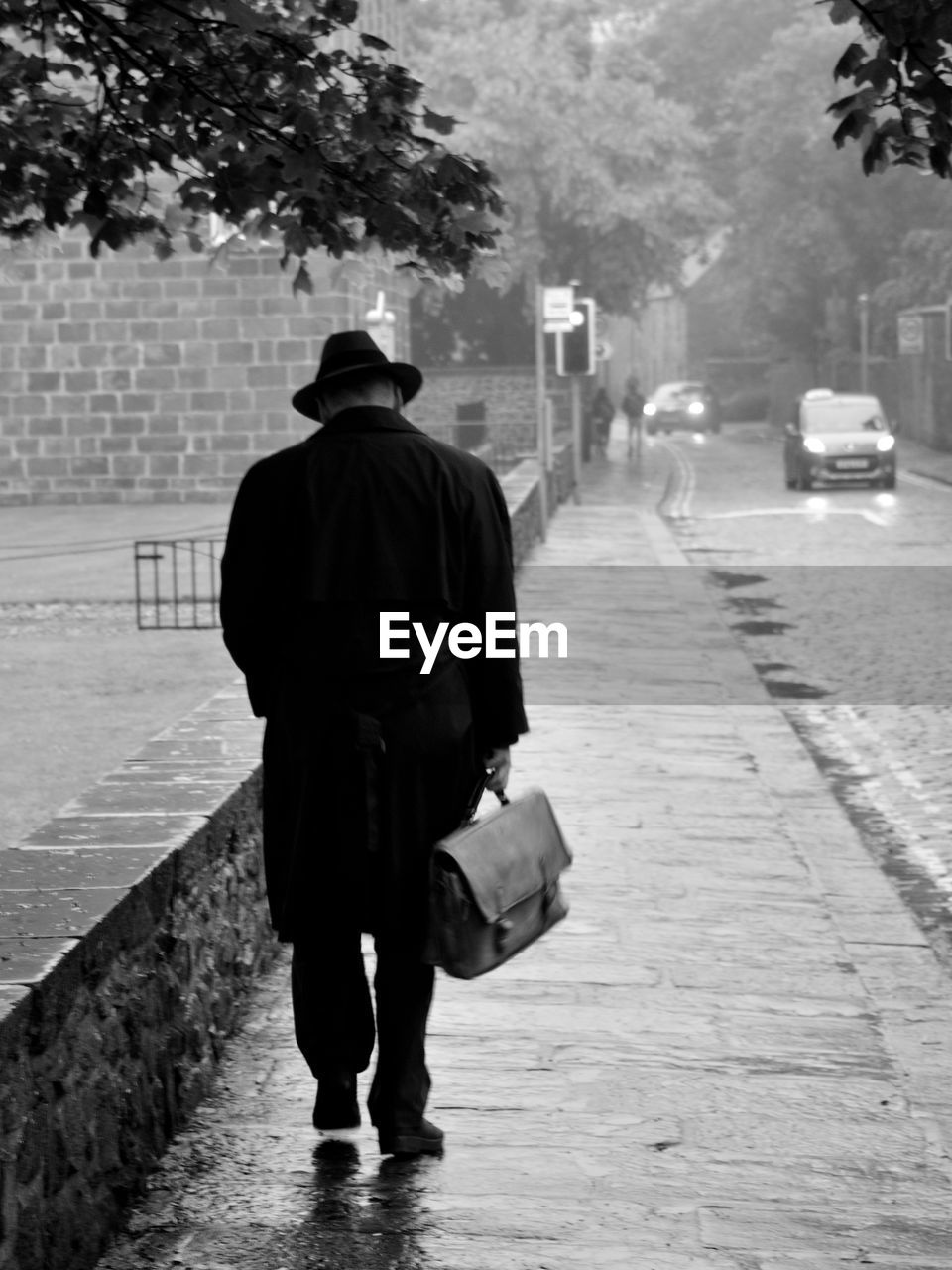 Rear view of man walking on footpath in city during rainy season