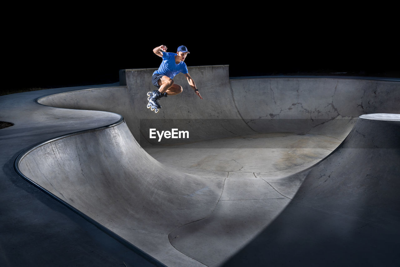 Young man practicing inline skating in skateboard park at night