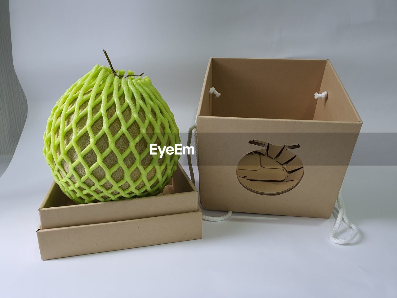 Close-up of melon fruit and paper box against white background