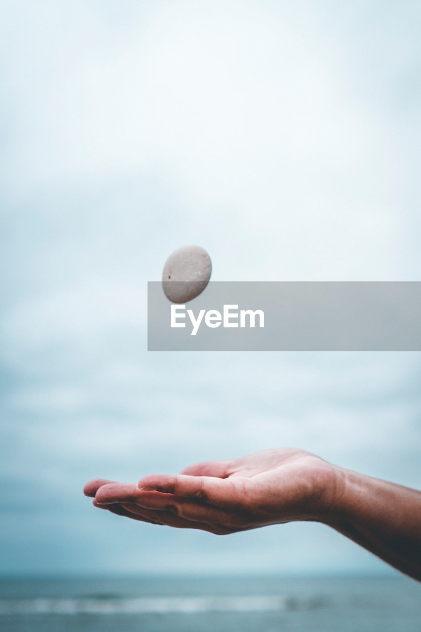 Close-up of hand catching stone against sea and sky