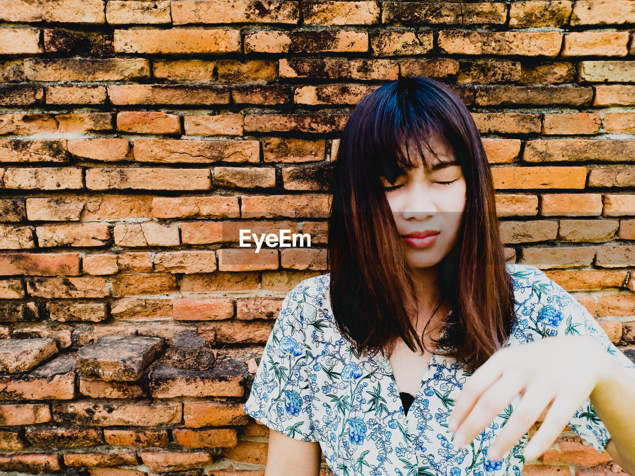 Young woman with closed eyes against brick wall