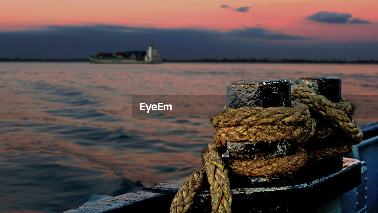 CLOSE-UP OF ROPE TIED ON BOLLARD AT HARBOR