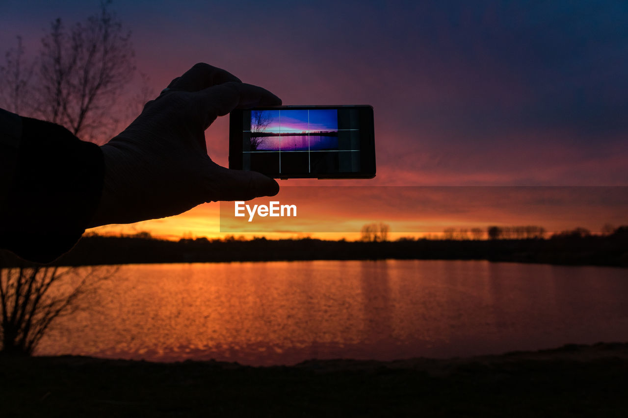 Man photographing sunset over lake through smart phone