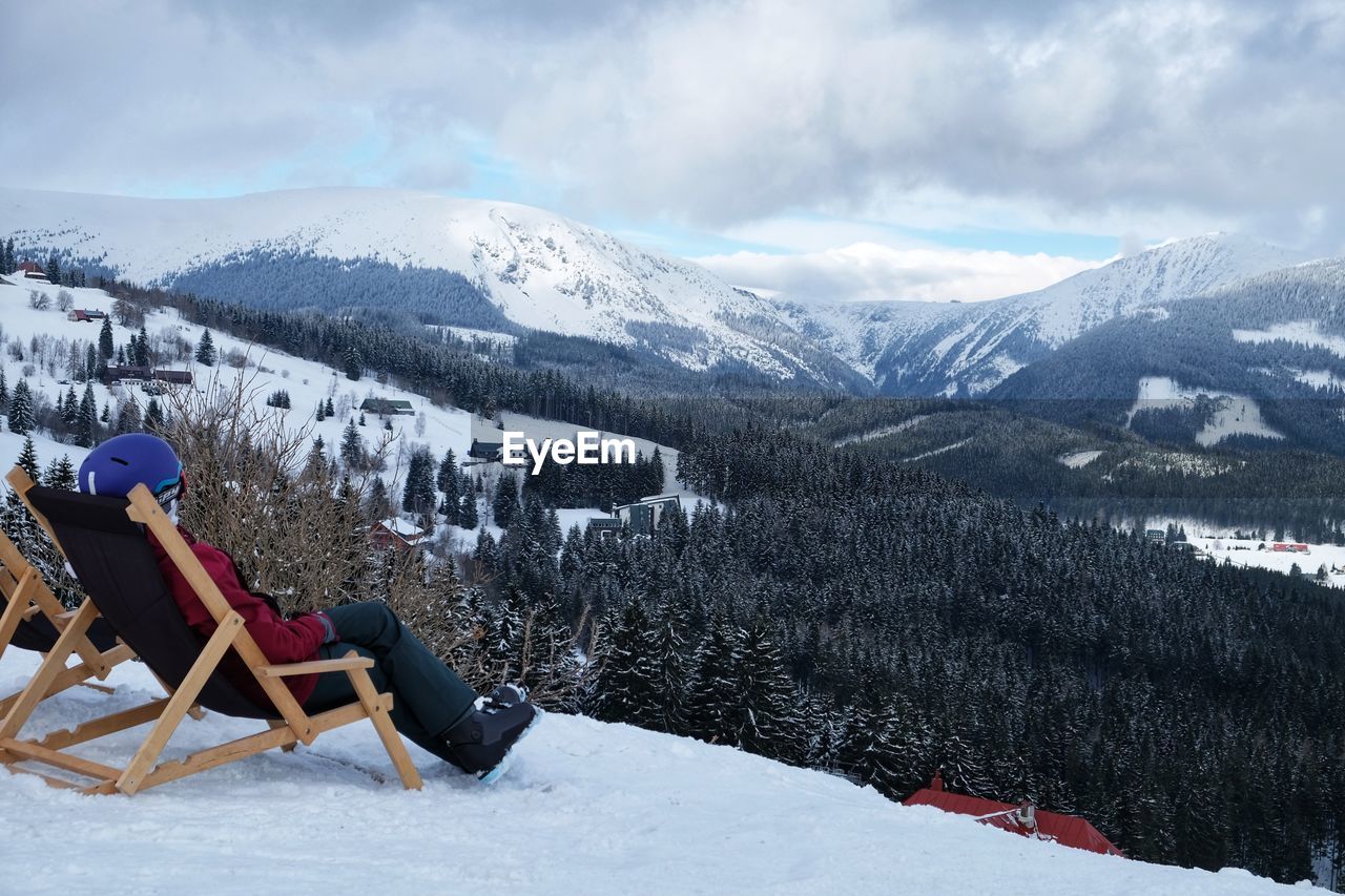 A woman resting admiring a ski lift over snowcapped mountains against sky