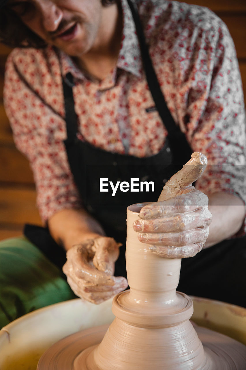 potter's wheel, adult, one person, indoors, pottery, craft, skill, occupation, creativity, art, women, holding, working, making, clay, food and drink, ceramic, craftsperson, person, lifestyles, young adult, front view, smiling, focus on foreground, expertise, apron, workshop