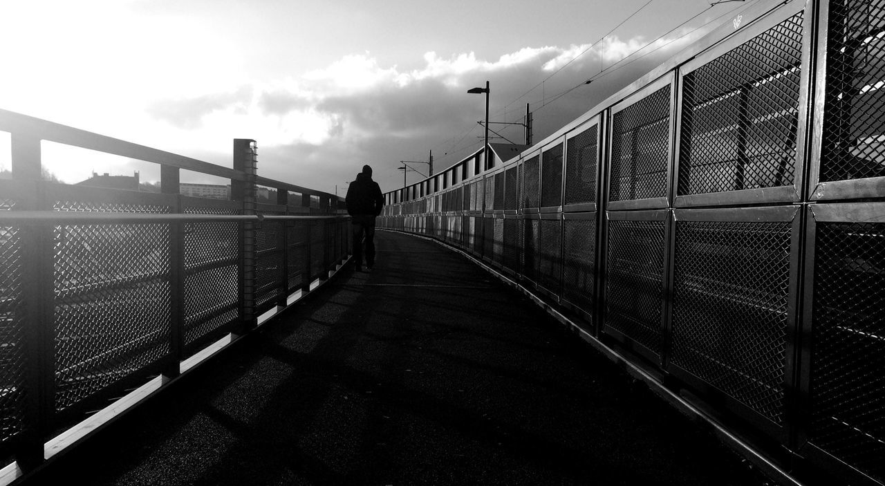 Silhouette person walking on bridge against cloudy sky
