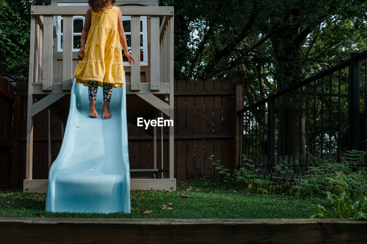 Little girl in yellow dress standing on blue slide