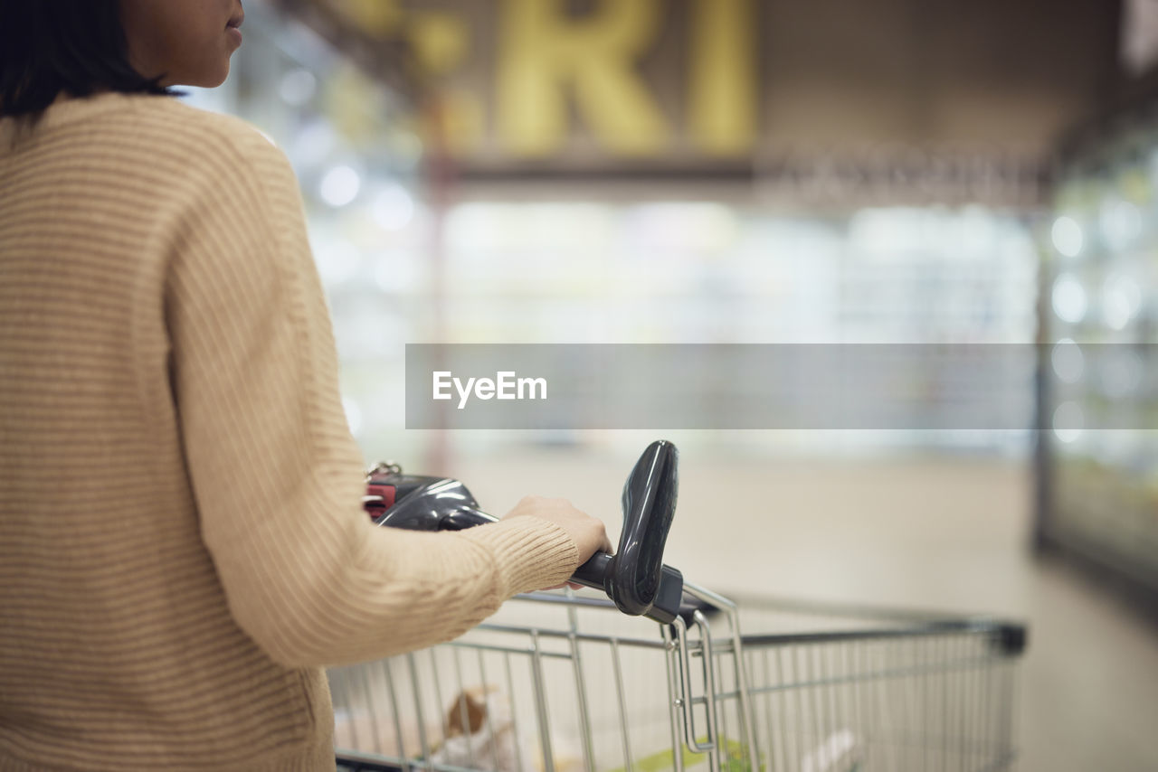 Mid section of woman pushing shopping trolley in supermarket