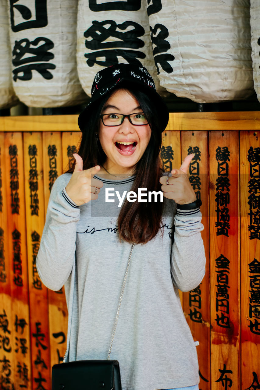 Portrait of happy young woman gesturing while standing against wall