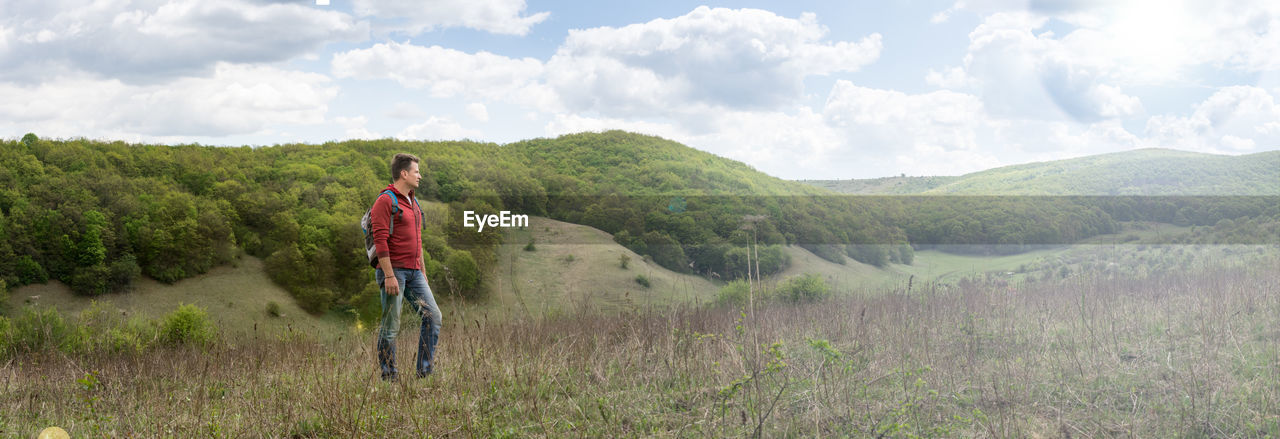 Adult man looks into the distance at the panorama of wooded hill