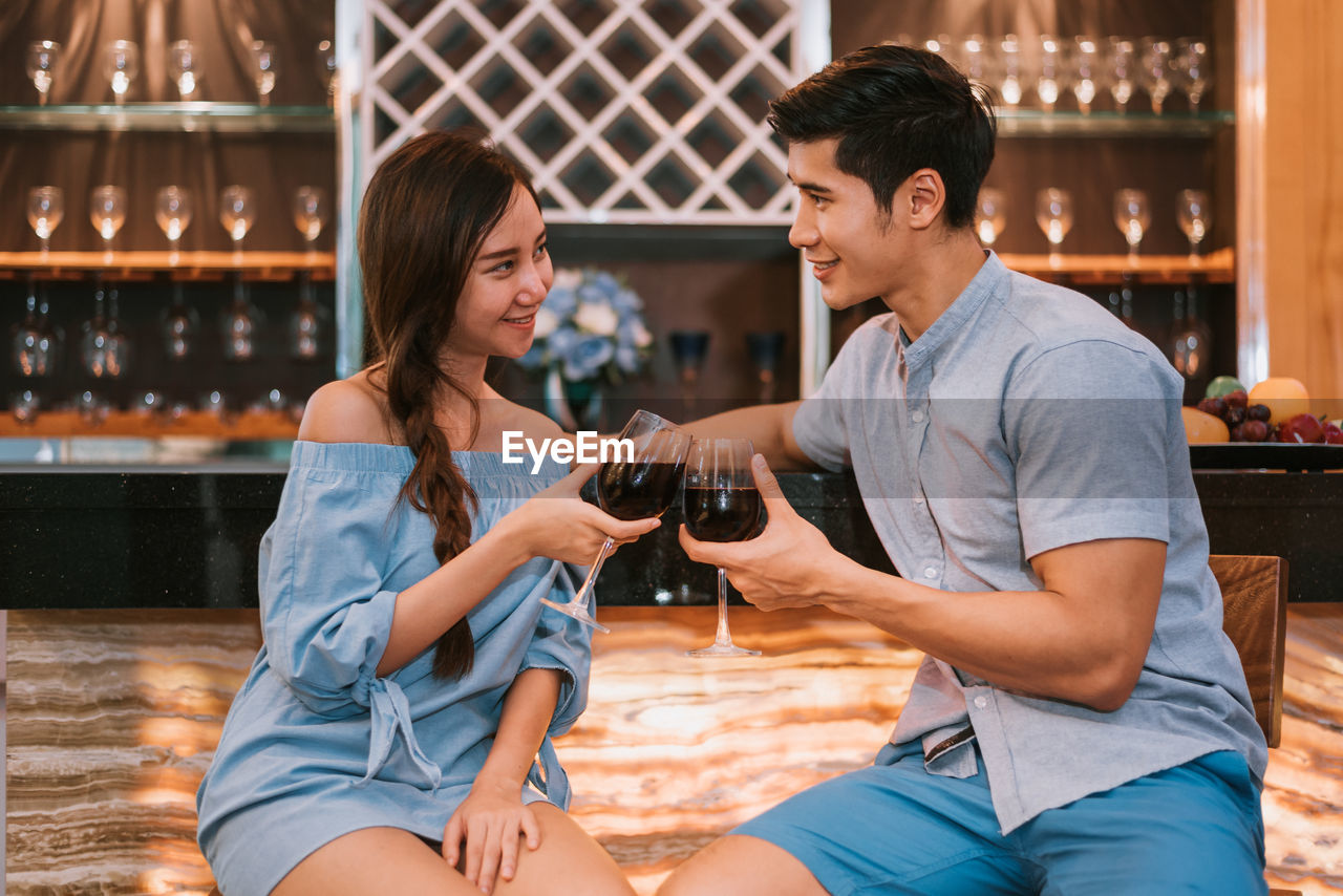 Young couple toasting drinks while sitting at bar counter